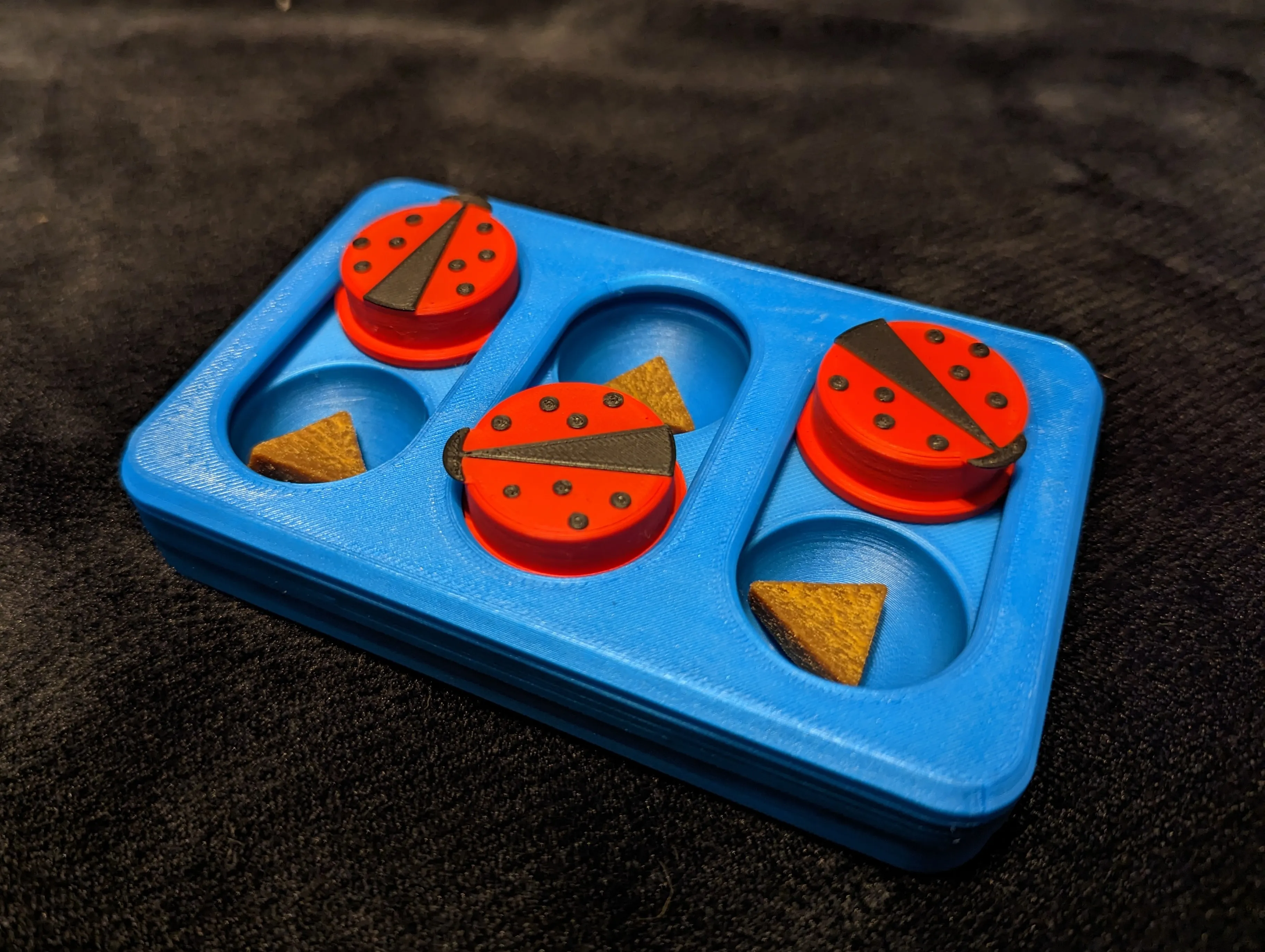 Juego interactivo azul impreso en 3D con huecos para golosinas cubiertos por fichas en forma de mariquita roja.